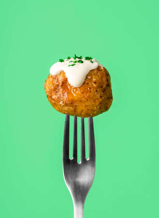 Roasted baby potatoes stuck on a fork, isolated on a green background. Single roasted potato with...