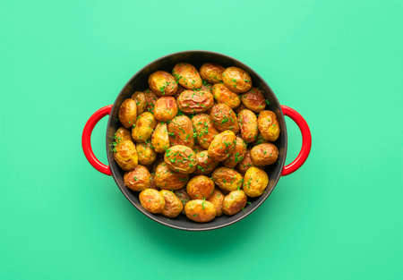 Roasted baby potatoes in a cast iron pan minimalist on a green table. Top view with a potato dish baked in a pan isolated on a colored backgroundの写真素材
