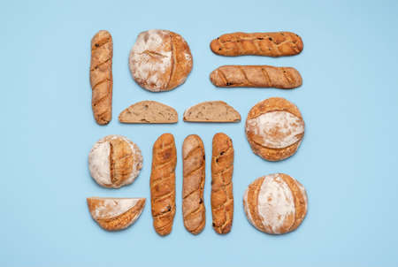 Food knolling with homemade sourdough bread. Round loaves and baguettes made with sourdough arranged symmetrically on a blue background.の写真素材