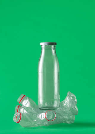 Glass bottle crushing plastic bottles as a concept for reusable containers. Alternative for the plastic bottles. Glass versus plastic bottles isolated on a green background.の写真素材