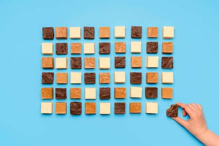 Eating homemade fudge with chocolate, caramel and white chocolate, isolated on blue background....