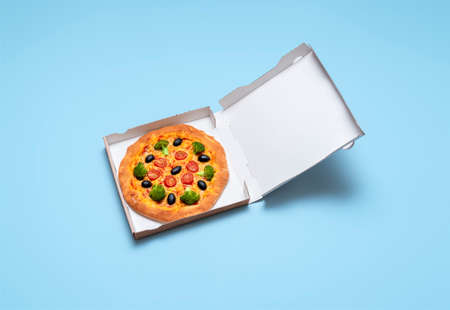 Top view with a vegan pizza in a cardboard box on a blue table. Pizza box isolated on a colored background. Pizza with vegan cheese, tomato sauce and broccoli.の写真素材