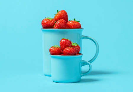Delicious organic strawberries in blue cups isolated on a colored background. Two cups with strawberries minimalist on the table.の写真素材