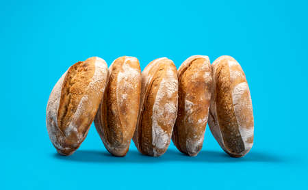 Delicious sourdough loaves of bread isolated on a blue-colored background. Sideview with a couple of home-baked loaves of bread on a blue table.の写真素材