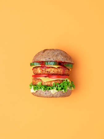 Side view from above with a vegan burger on an orange table. Homemade burger with soya patties as a meat substitute, vegan cheese and remoulade, and fresh vegetables.の写真素材