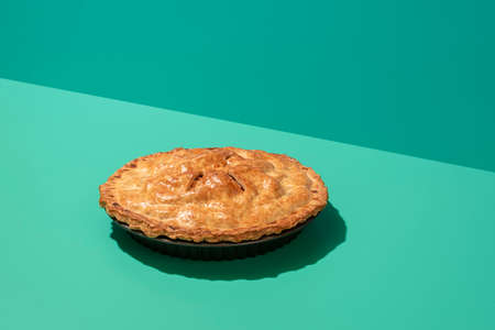 Freshly baked apple cake in minimalist on a green table with harsh shadow. Homemade apple pie with a...