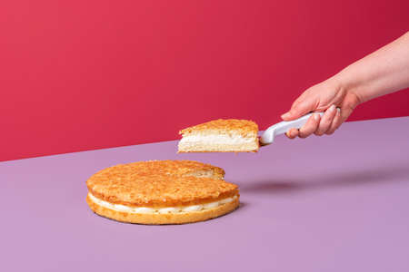 Woman's hand taking a slice of almond cake. Delicious almond pie with whipped cream minimalist on a purple table.の写真素材