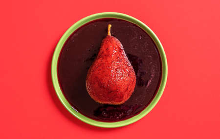 Top view with a single pear on a plate in red wine sauce. Pear boiled in wine, minimalist on a red background.の写真素材