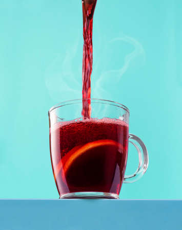 Pouring hot wine in a glass mug against a blue cyan background. Christmas mulled wine in a mug isolated on a colored background.の写真素材