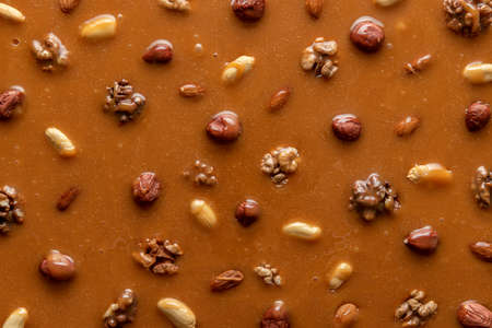 Melted caramel sauce with assorted nuts, full-frame image. Top view of peanut brittle ingredients....