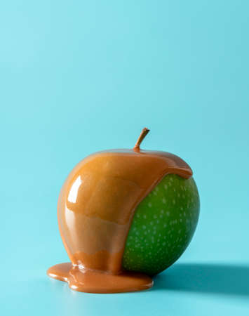 Green apple with caramel sauce isolated a blue background. Delicious caramel apple minimalist on a blue table.の写真素材