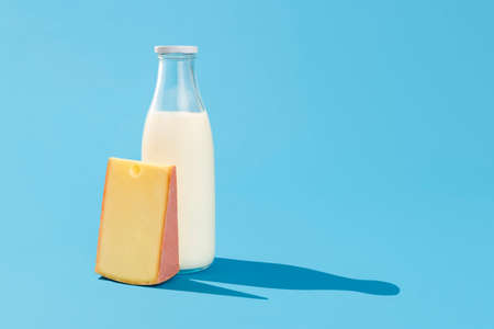 Bottle of milk and a slice of swiss cheese isolated on a blue background. Fresh milk in a glass bottle and a piece of cheese in bright light on a blue-colored table.の写真素材