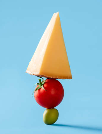 Close-up with a slice of cheese, tomato, and a green olive stacked one above each other. Swiss...
