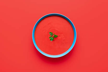 Above view with tomato cream soup in a blue bowl minimalist on a red table. Bowl of delicious soup isolated on a colored background.の写真素材