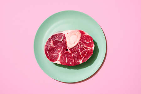 Above view with a single beef steak on a green plate, minimalist on a pink background. Top view with a slice of raw meat on a colorful tableの写真素材