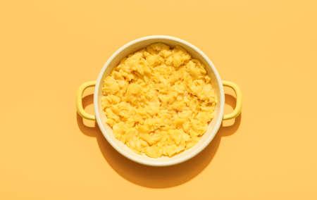 Above view with a portion of scrambled eggs in an enamel plate isolated on an orange background....