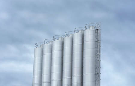 Stainless steel milk tanks at a modern dairy farm. Large storage tanks used in the beverage industry against a cloudy sky.の写真素材