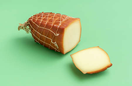 Close-up with a big chunk of smoked cheese on a green table. Smoked cheese string wrapped with a single sliced piece, minimalist on a green background.の写真素材
