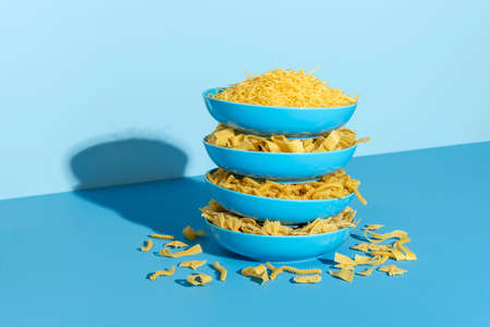 Plates with uncooked pasta stacked one above each other  on a blue table. Variety of pasta in blue...