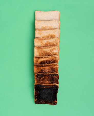 Top view with a variety of toasted bread, from unroasted to extremely burnt, aligned in a row on a green table.の写真素材