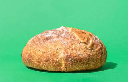 Close-up with a whole bread minimalist on a green background. Home-baked white bread in bright...