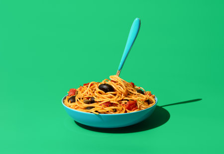 Classic italian pasta, spaghetti puttanesca, minimalist on a green table. Delicious vegetarian pasta dish, spaghetti with tomato sauce, olives, and capers.の写真素材