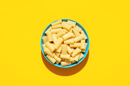 Pasta rigatoni cooked and with no sauce, top view on a yellow table. Plain pasta bowl minimalist on a vibrant colored background.の写真素材