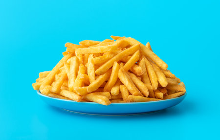 Plate with homemade french fries, minimalist on a blue table. Close-up with delicious fried potatoes...