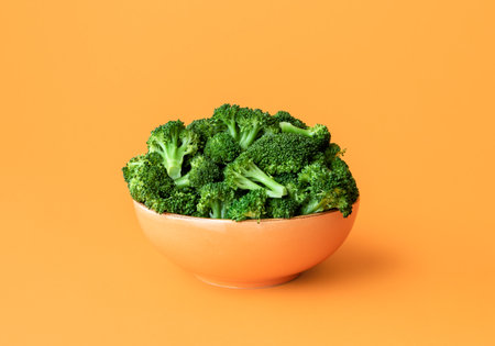 Bowl with boiled broccoli minimalist on an orange table. Close-up with cooked green broccoli in an...