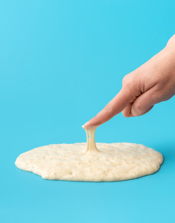 Woman is testing the sourdough yeast with one finger, minimalist on a blue table.