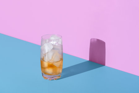 Glass with ice cubes and tea in bright light, minimalist on a blue table. A refreshing drink, iced tea in a frosty glass.の写真素材