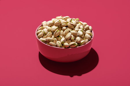 Pink bowl with roasted and salted pistachio minimalist on a magenta table. Bowl with pistachio isolated on a vibrant-colored backgroundの写真素材