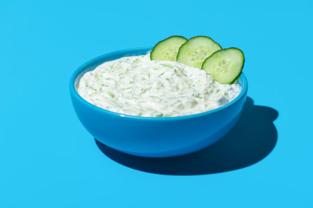 Homemade tzatziki sauce in a blue bowl in bright light on a vibrant colored table. Bowl with tzatziki sauce isolated on a blue background.の写真素材