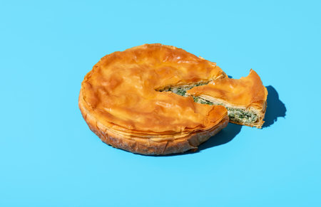 Homemade savory pie with spinach and cheese, balkan recipe, minimalist on a blue table. Delicious spinach cake made with phyllo doughの写真素材