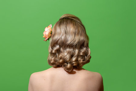 Back view of a blonde woman with retro-style hair and naked shoulders, minimalist on a green...