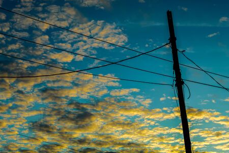 Electric post silhouette with a beautiful sky behind, clouds with orange light of the sunrise.の写真素材