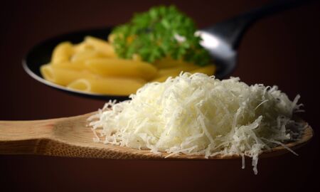 Parmesan cheese grated on a spoon with a skimmer full of pasta.の写真素材