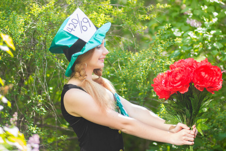 Portrait of a beautiful young woman in a costume of the Mad Hatter in nature  Girl posing with a bouquet of red peoniesのeditorial素材