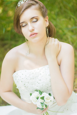 Portrait of a beautiful young bride in nature  Young woman holding a small bouquet of white roses in their handsの写真素材