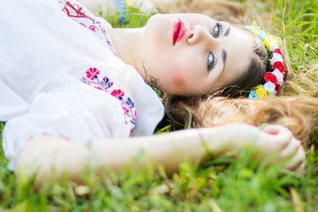Outdoor portrait young woman with long brown hair  The girl floral accessories, she poses lying on the grass in the parkの写真素材