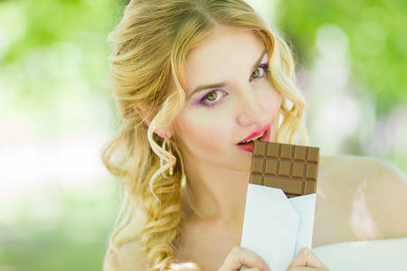 Portrait of a chocolate loving young blonde beauty on the background of trees in the park. Soft focusの写真素材