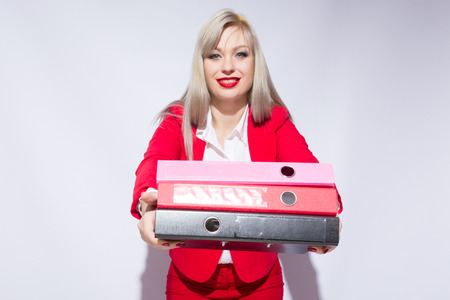 Portrait of a beautiful secretary in a red suit with folders in handsの写真素材