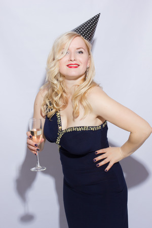 Beautiful young blond woman at the party. The girl is dressed in evening dress with a festive cap, in her hand holds a glass of champagne
の写真素材