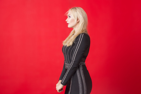 Image of young happy blonde woman in black dress over red background.の写真素材