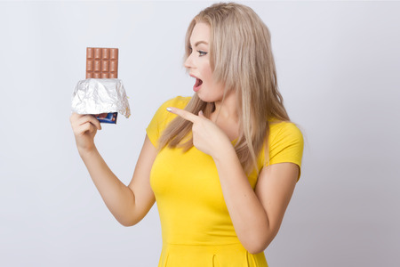 Smiling blondhair woman in yellow dress over grey background. She holding chocolate in her handsの写真素材