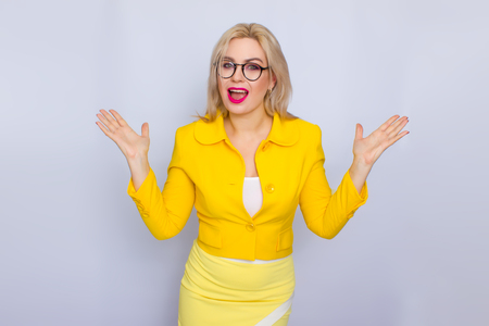 Beautiful blonde business woman wearring eyeglasses and yellow suit over white background in studioの写真素材