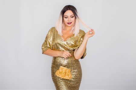 Charming young blonde haired woman wearing elegant gold evening dress and holding gold color clutch in her hands. Fashion shot. White backgroundの写真素材