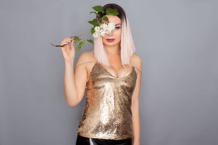 Young stylish blonde woman dressed in a golden top holds in her hands a branch of a white lilac. studio shotの写真素材