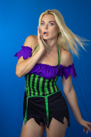 Young beautiful blonde woman in a witch costume on a blue background. Short dress, long hair. Halloween concept. Soft focusの写真素材