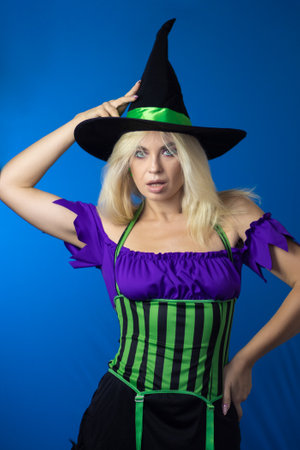 Young beautiful blonde woman in a witch costume on a blue background. Short dress, long hair, black...